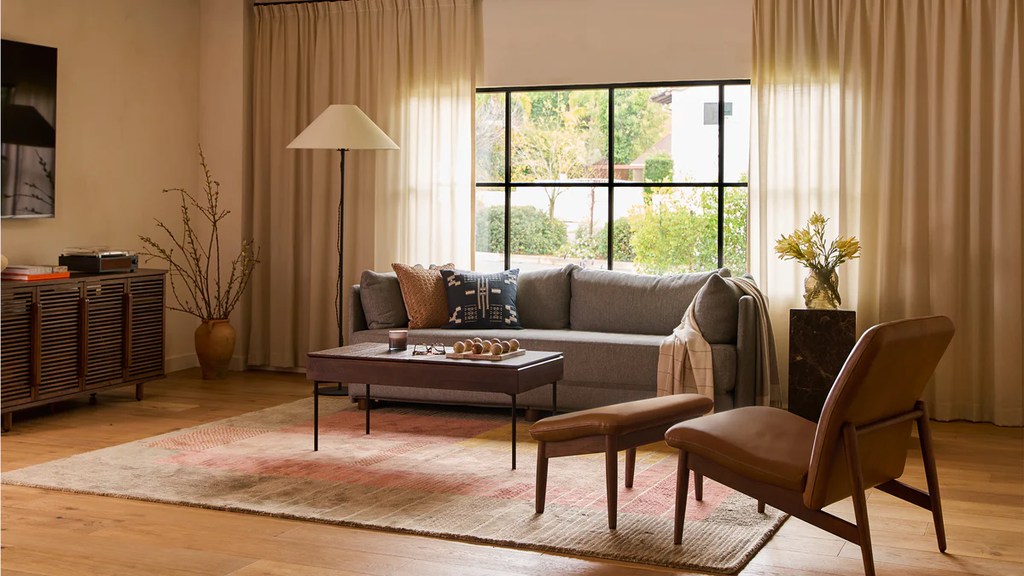 Burrow Shift Sleeper Sofa near a rectangular coffee table, a round side table with a plant on top, an accent chair and a tufted media console with some books and a disc player on top in a mid century modern living room
