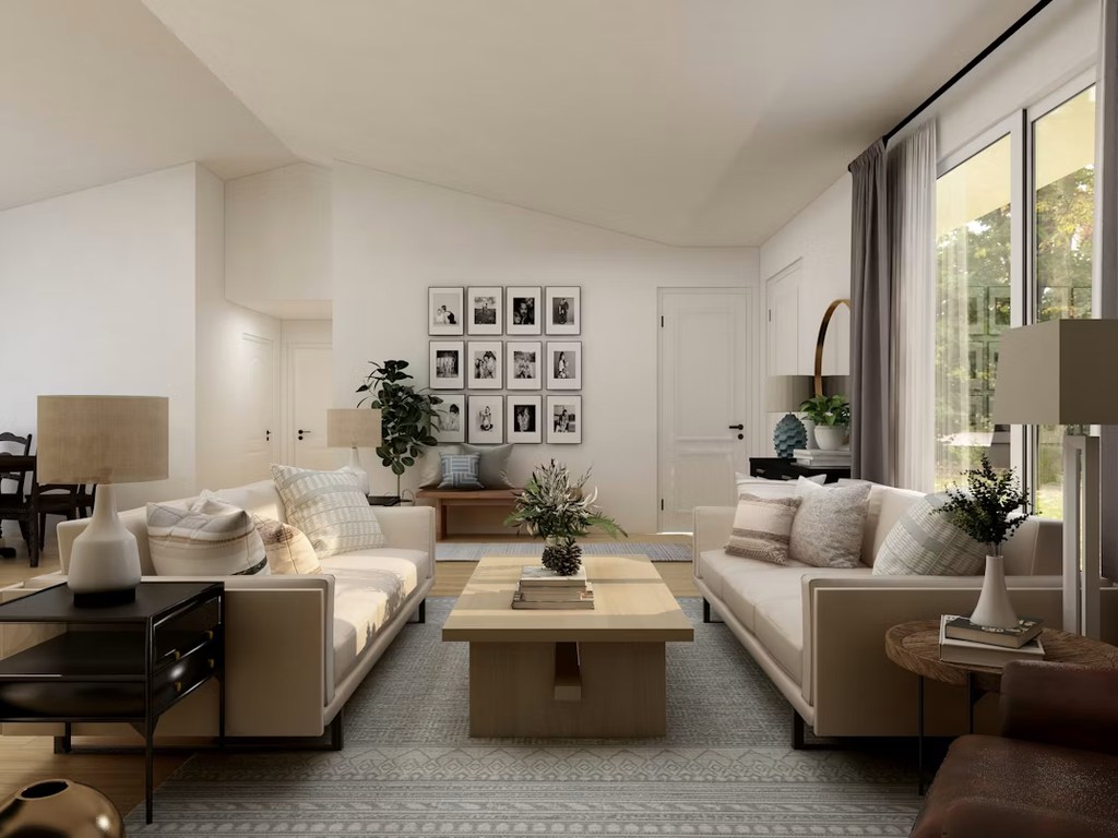 Bright apartment living room with two cream sofas, a square coffee table, large windows, and neutral decor creating an open seating layout.