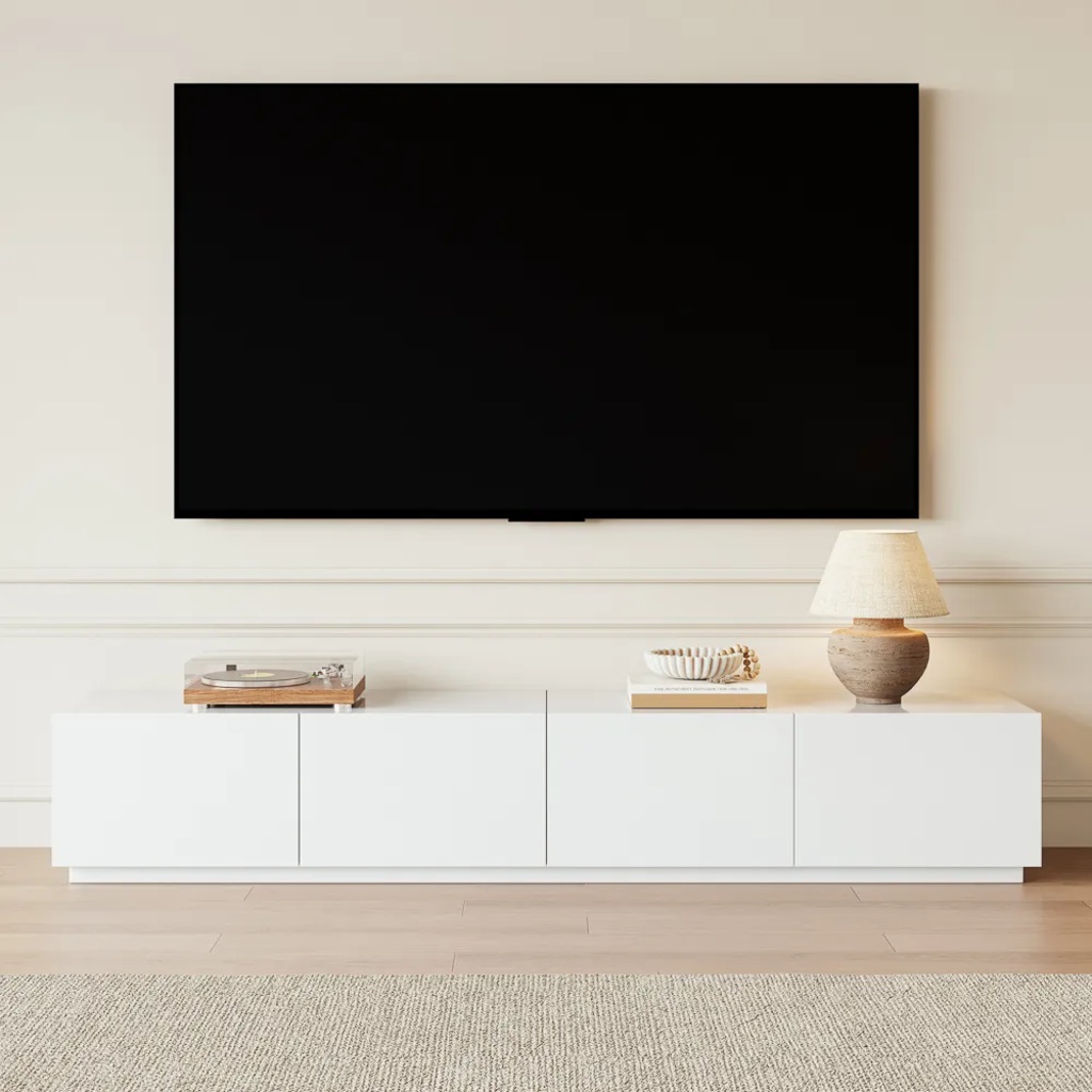 POVISON Modern Large Matte TV Stand in white with a disc player, a book and a lamp on top against a white wall with a mounted tv in a modern and minimalist living room