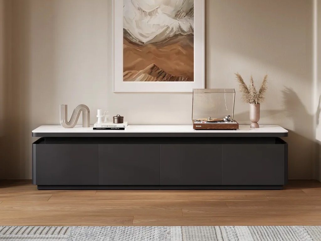 a black and white media console with a disc player, a vase, some books and decorations on top against a white wall with a mounted painting in a minimalist living room