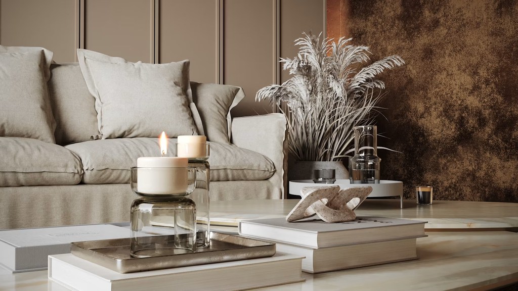 Modern coffee table styled with candles, books, sculptural decor, and dried grass beside a neutral sofa in a warm contemporary living room.