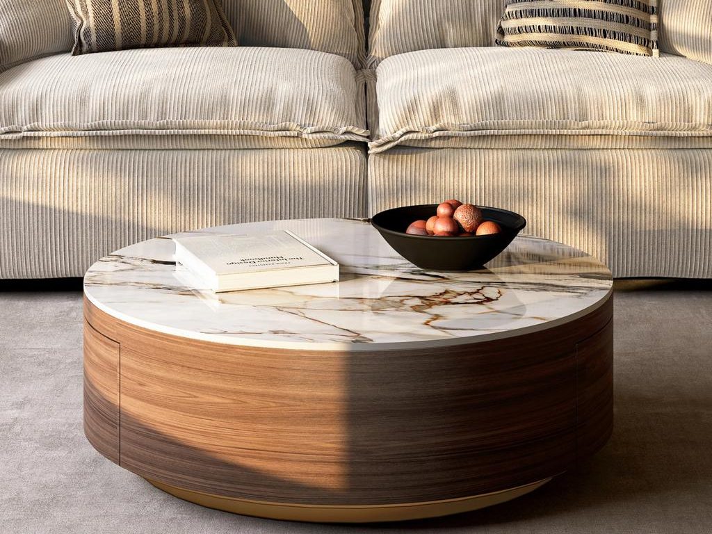 a round coffee table with sintered stone and a book on top near a white tufted sofa