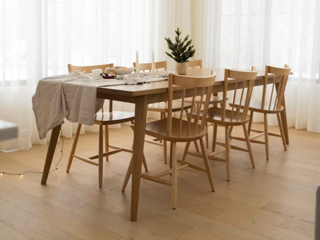 an oak wood dining table with six oak dining chairs in a bright and minimalist living room with wood floor