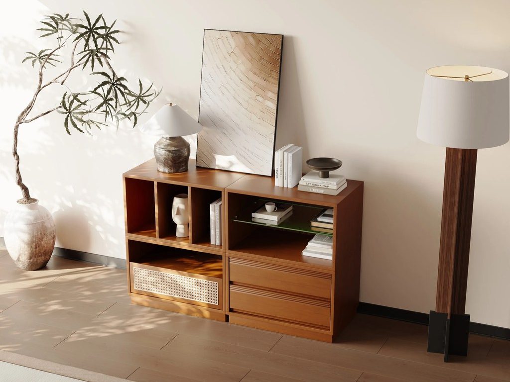 a cherry wood console table with four blocks for books with a lamp, a painting and decorations on top beside a floor lamp and a plant in a bright area