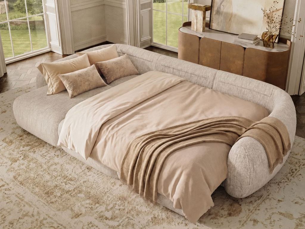 Neutral upholstered bed with beige bedding and a fringed throw blanket in a bright room with tall windows, a curved sideboard, and abstract wall art.
