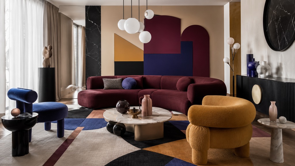 Postmodern living room with a curved burgundy sofa, cobalt blue and mustard chairs, geometric rug, sculptural tables, and globe lighting.