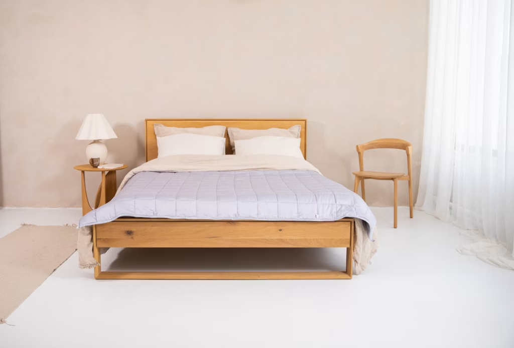 Minimalist wooden bed centered in a white room, demonstrating furniture footprint and ample walking space around the frame.