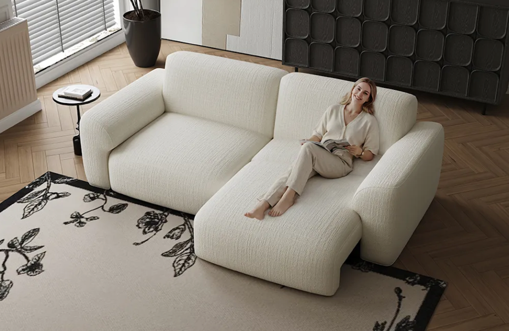 A woman relaxing and reading on a cozy cream boucle sofa with one half extended forward into a chaise longue.