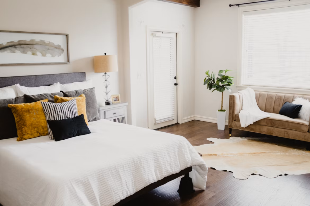 Cozy bedroom layout featuring a white bed with textured pillows and a chic velvet sofa in a sunlit corner.