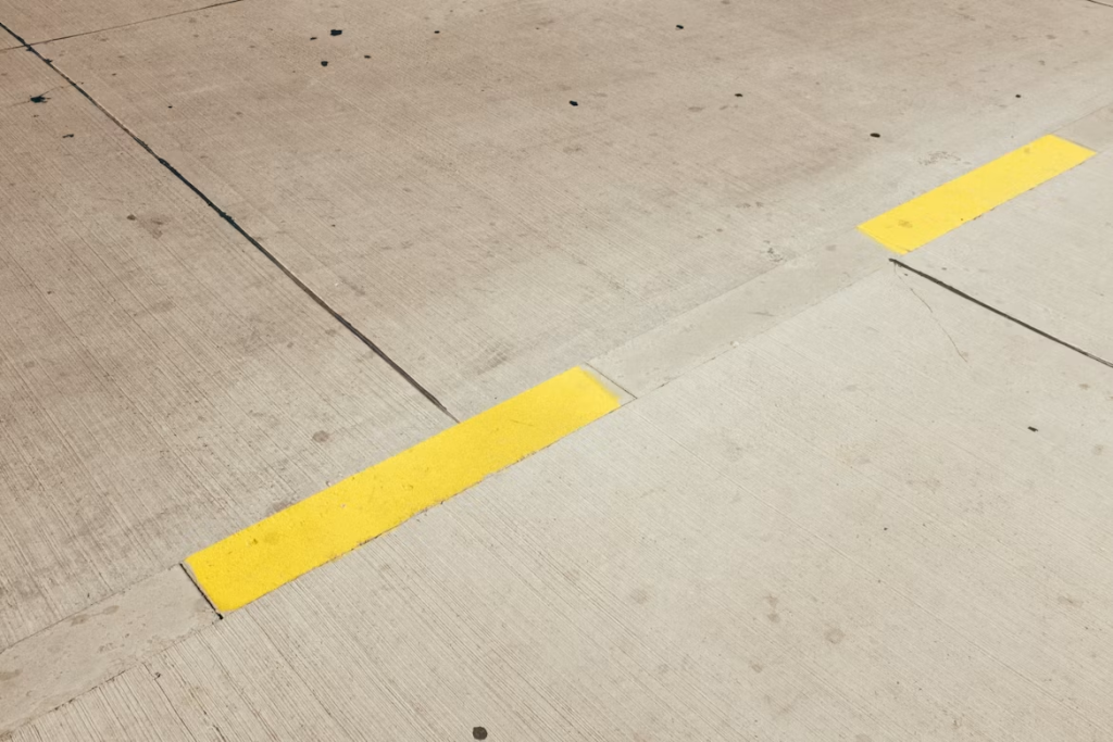 Bright yellow tape on floor running diagonally across a textured, grey concrete pavement background.