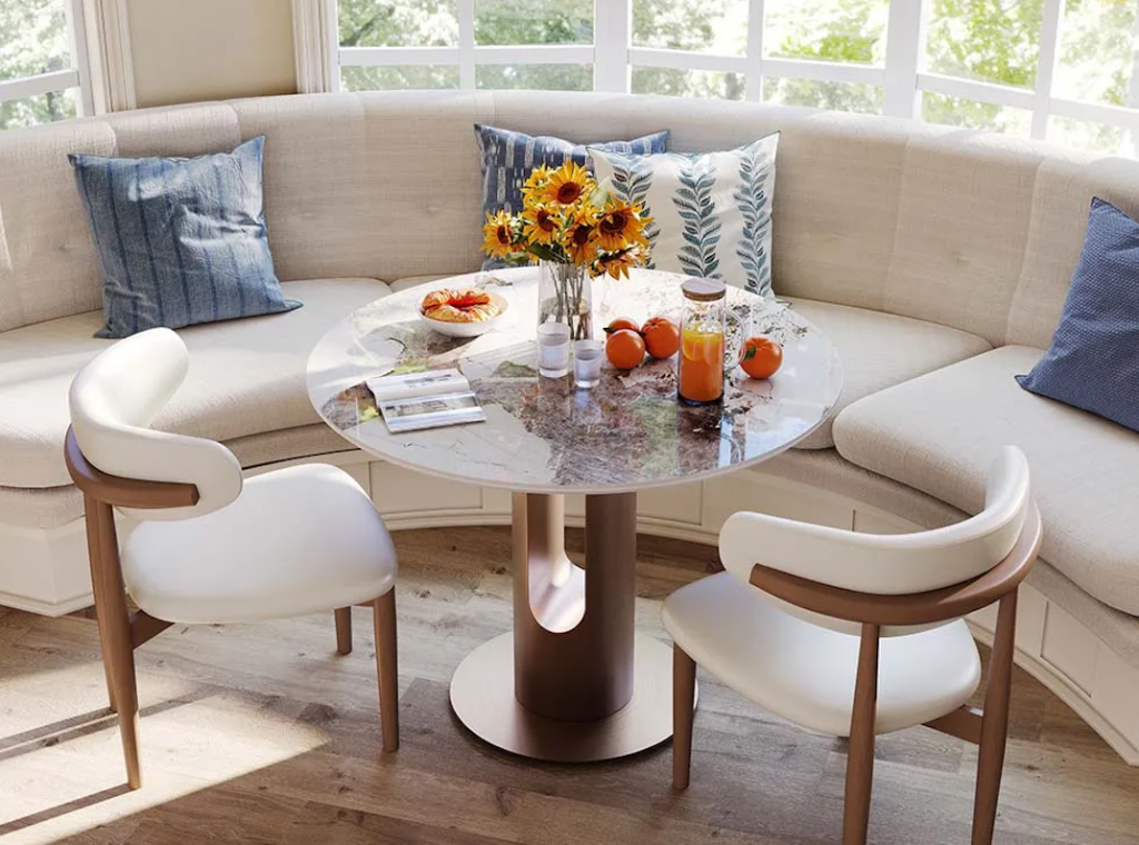 Elegant cream upholstered curved corner bench dining set styled with a marble table and sunflowers.
