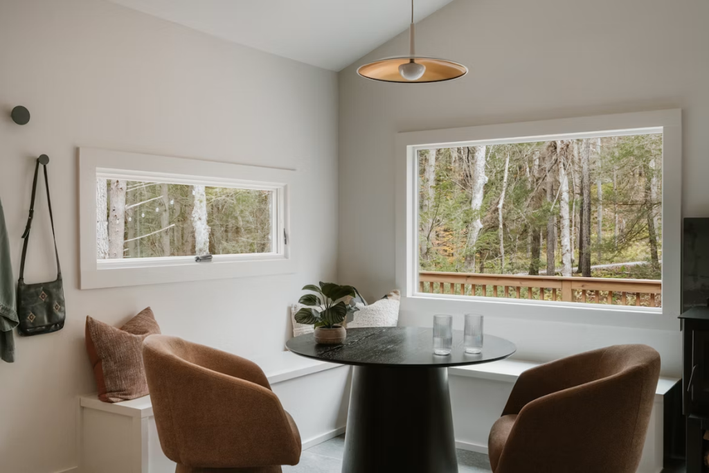 Modern minimalist white corner bench dining set paired with a dark round table near large windows.