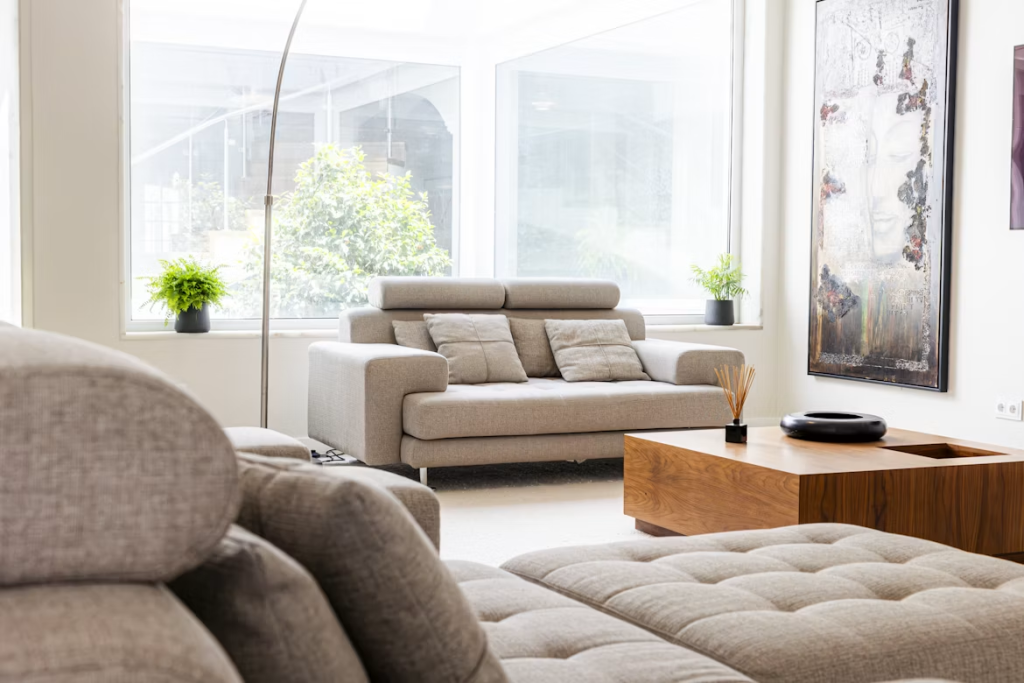 Cozy light grey sofa with adjustable headrests in a sunlit living room featuring large windows and wood coffee table.