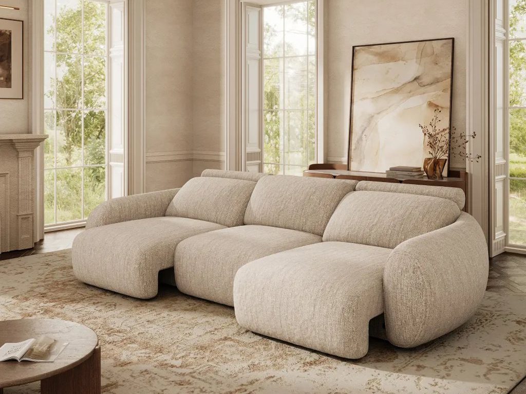 Beige oversized power sleeper sofa in a bright contemporary living room with tall windows, a glass chandelier, and a neutral patterned rug.