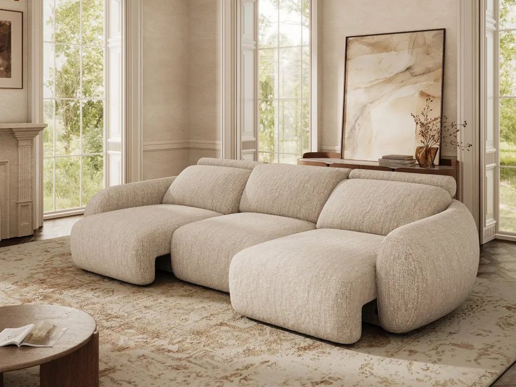 Beige oversized power sleeper sofa in a bright luxury living room with tall windows, a chandelier, and a neutral patterned rug.