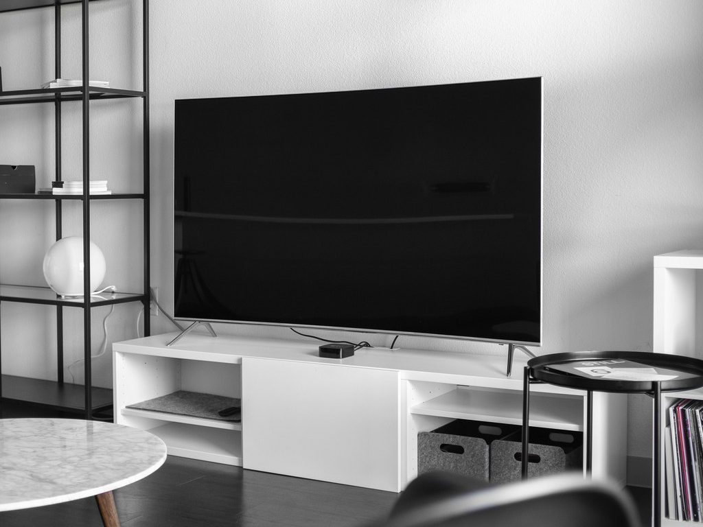 Low-profile white TV stand with open shelves beneath a large TV in a modern black-and-white living room.