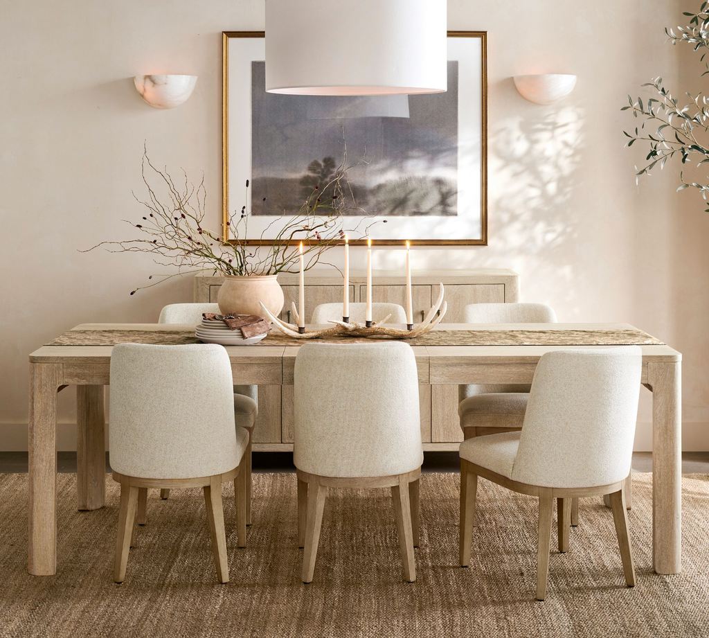 Large light wood dining table with six upholstered chairs in a neutral dining room.