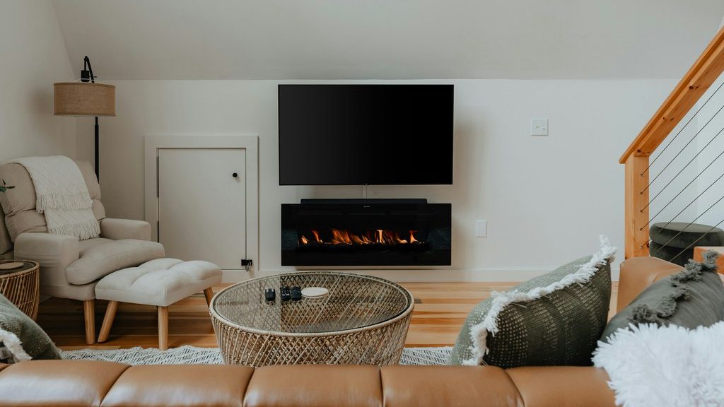 Wall-mounted TV above a modern electric fireplace in a cozy living room with neutral seating.