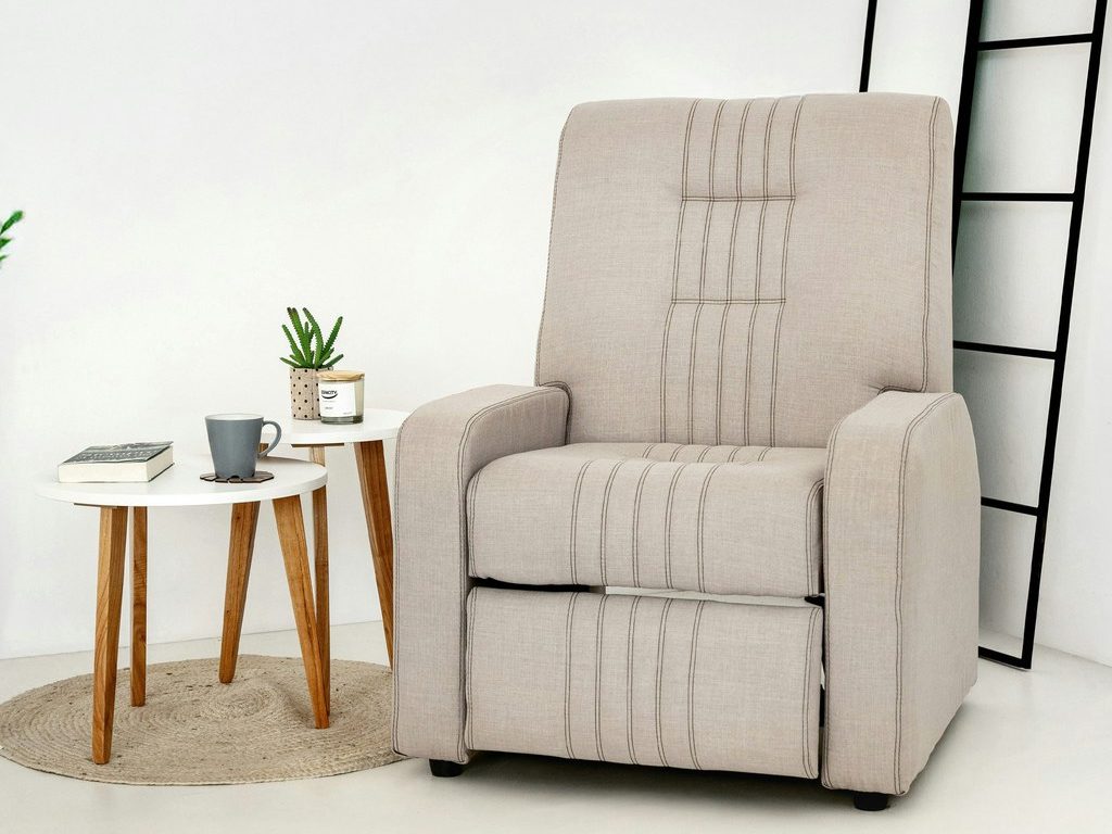 Beige upholstered recliner with stitched detailing beside two round wood-leg side tables in a minimalist living room.