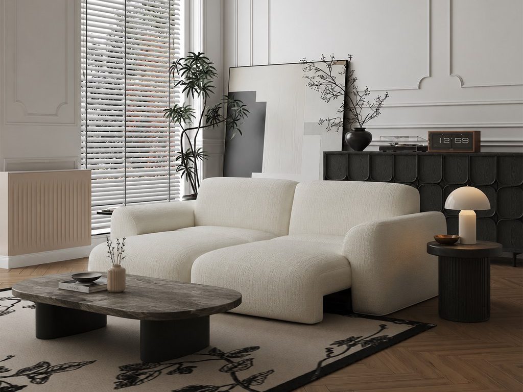 Cream sofa bed styled with a dark stone coffee table, round side table, table lamp, and botanical area rug in a modern living room.