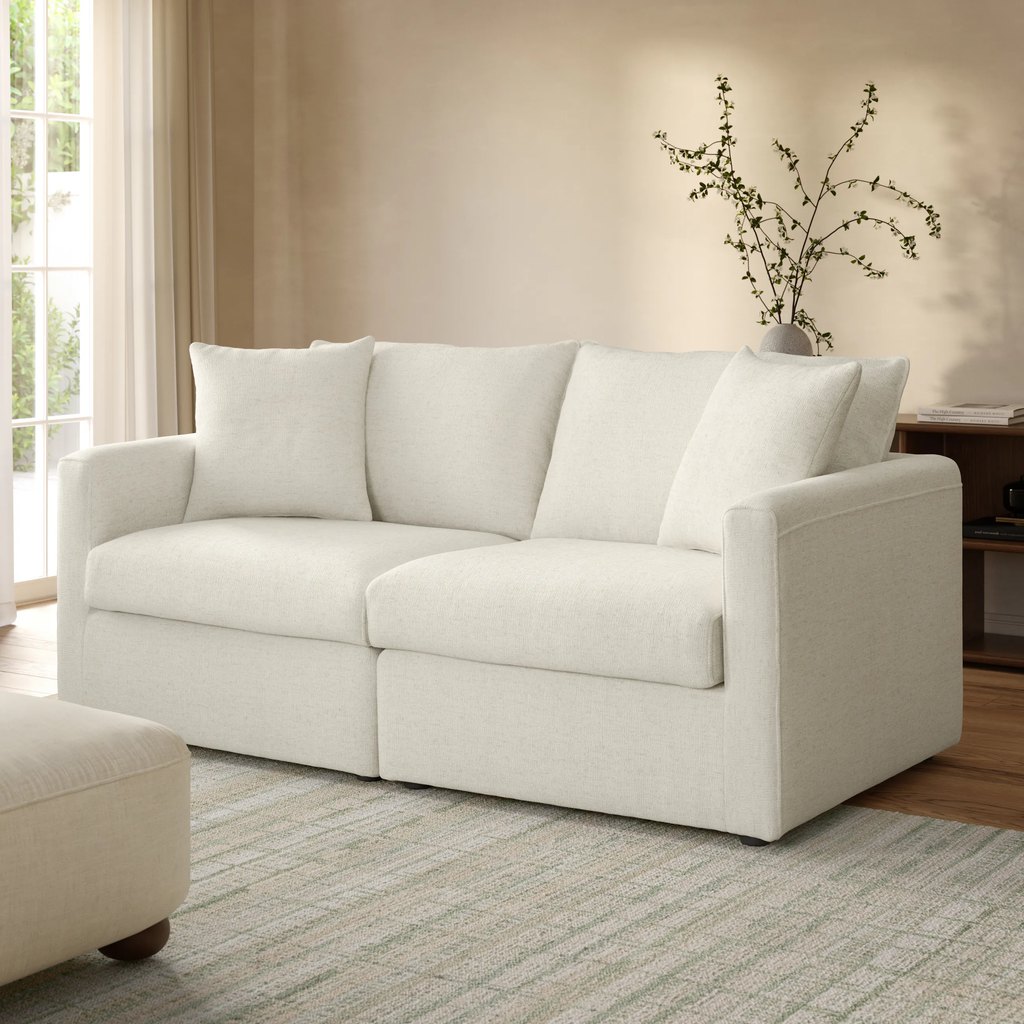 White modular loveseat with loose back cushions in a bright, neutral living room.