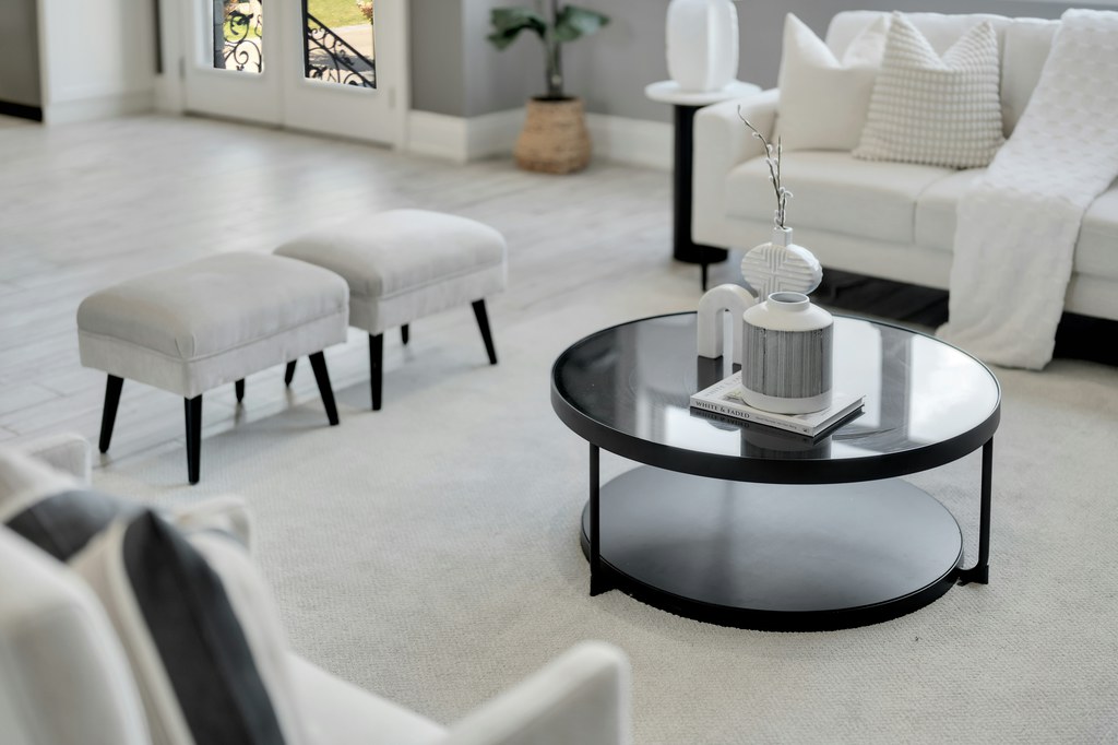 Black round coffee table with a lower shelf in a bright modern living room with white seating and upholstered stools.