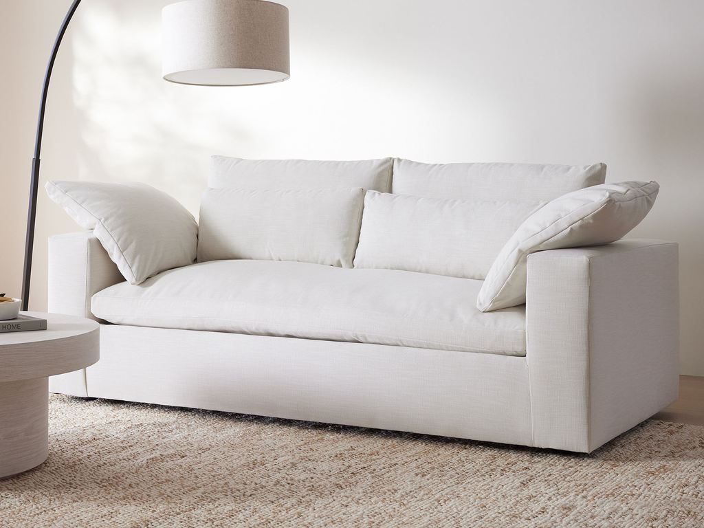 White modular sleeper sofa with oversized cushions, a curved floor lamp, and a textured neutral rug in a minimalist contemporary living room.