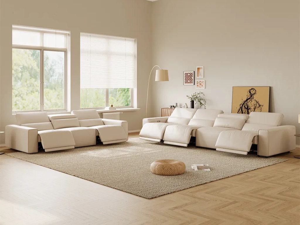 Spacious modern living room with matching white reclining sofas, extended footrests, large windows, and an open floor layout.