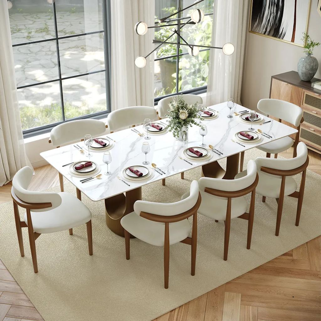Large white rectangular dining table set for eight with upholstered chairs in a bright dining room.