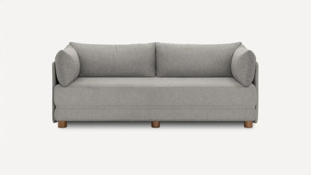 Gray upholstered sleeper sofa with rounded bolster pillows and short wooden feet on a white background.