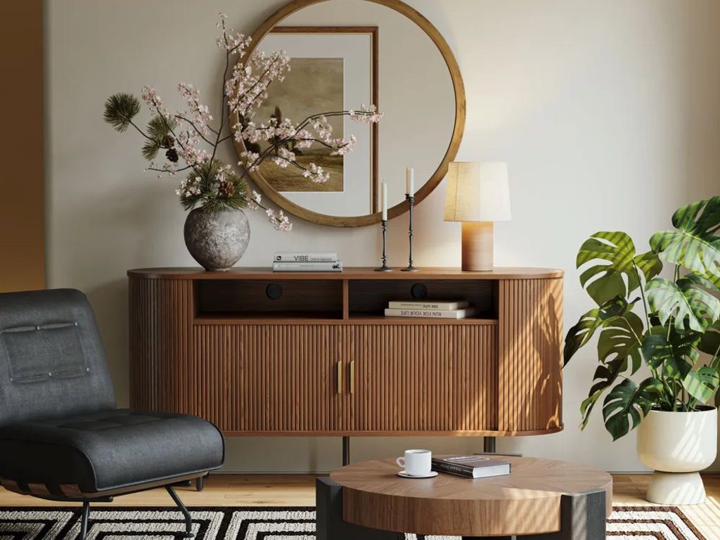 Modern living room with a wood sideboard, round mirror, candleholders, table lamp, lounge chair, and round coffee table.
