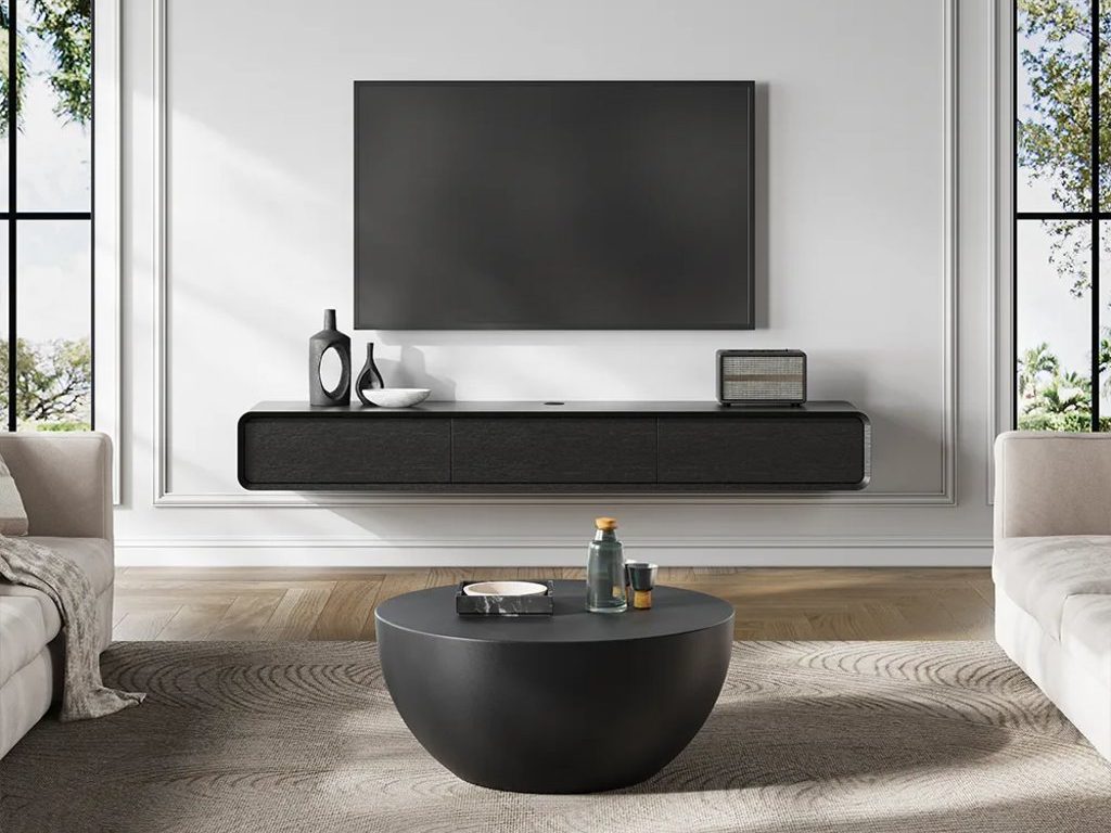 Black floating TV stand beneath a wall-mounted TV in a bright modern living room with neutral seating.