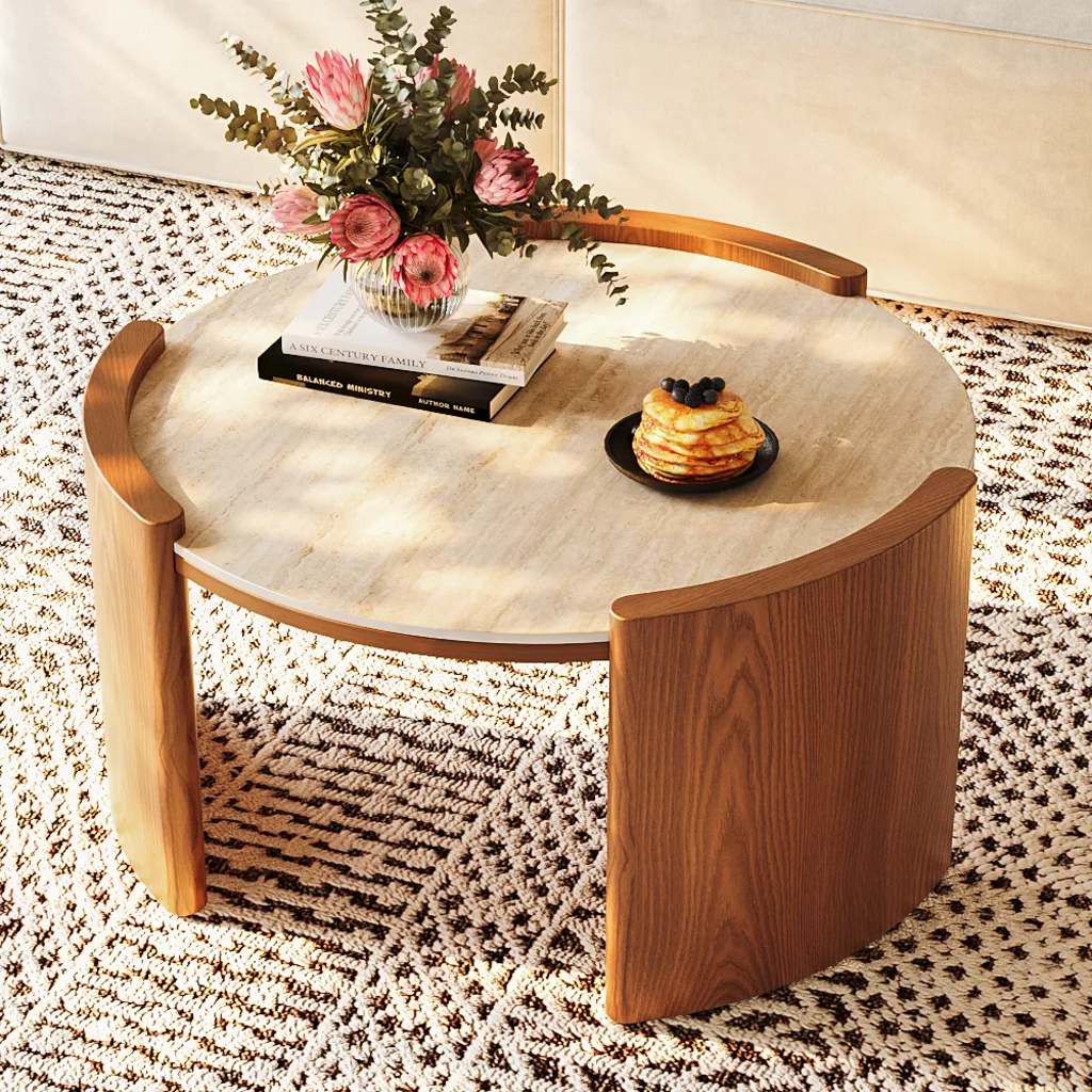 Round travertine-look coffee table with a sintered stone top and curved walnut tripod base in a bright living room.