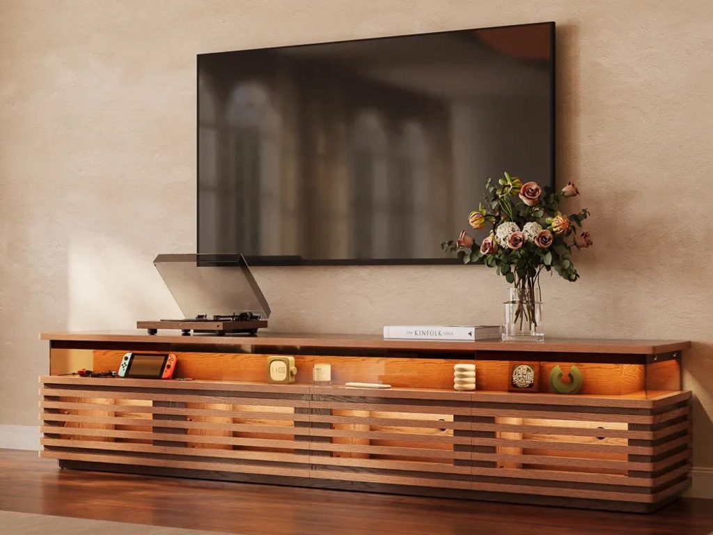 Wall-mounted TV above a warm wood slatted media console, styled with a record player, flowers, books, and small decor in a cozy modern living room.