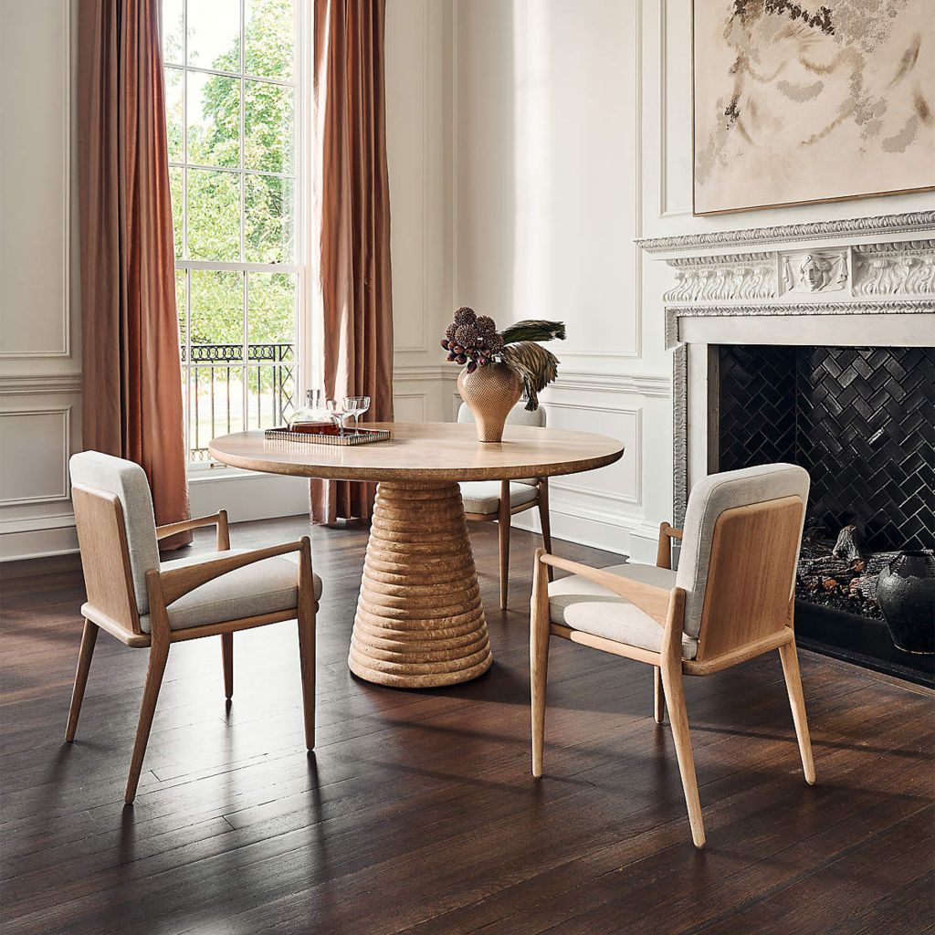 Round wooden designer dining table with a ribbed pedestal base and upholstered chairs in an elegant dining room.