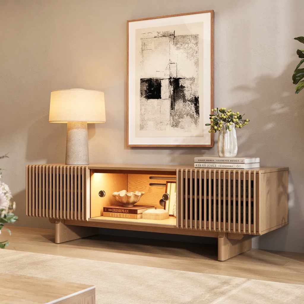 Light wood slatted media console with integrated warm LED lighting, a table lamp, framed abstract art, and a neutral living room wall.