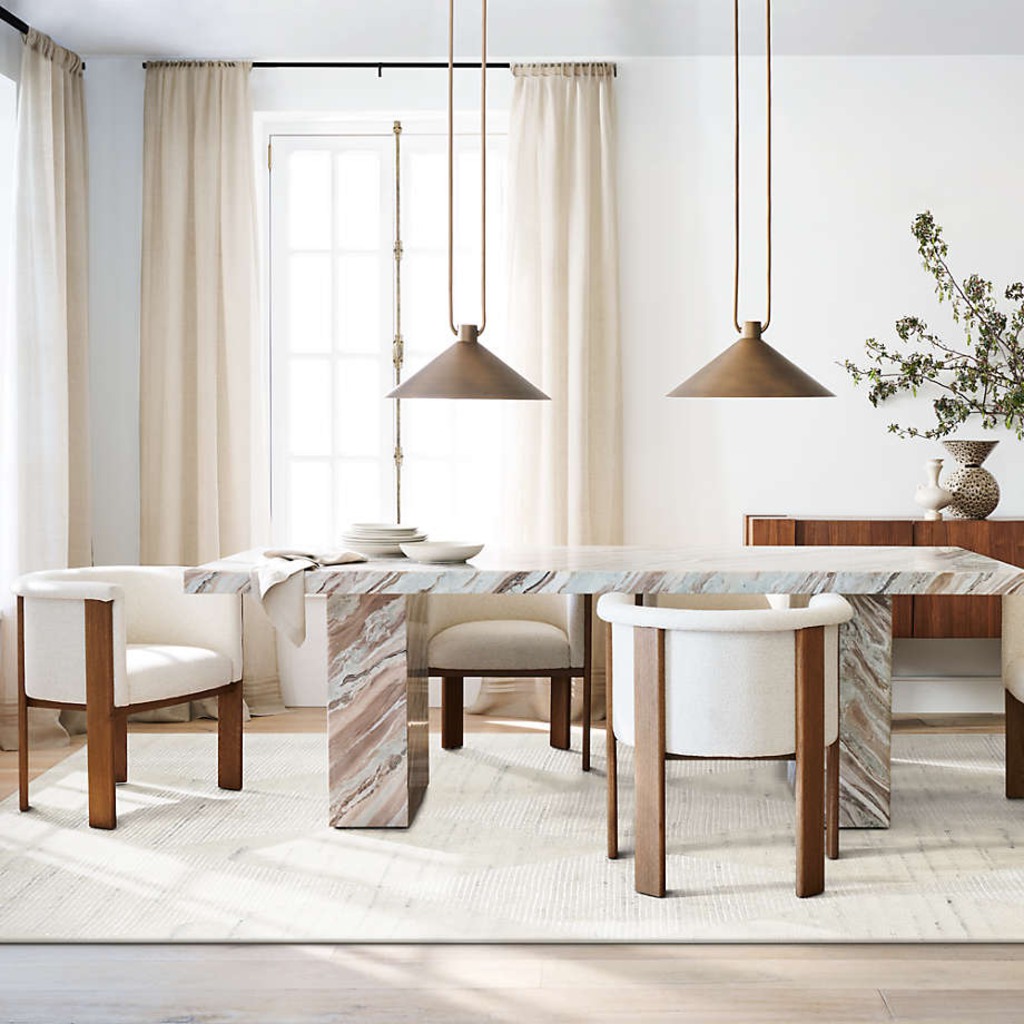 Rectangular marble designer dining table with block legs, upholstered wood chairs, and twin pendant lights in a bright modern dining room.