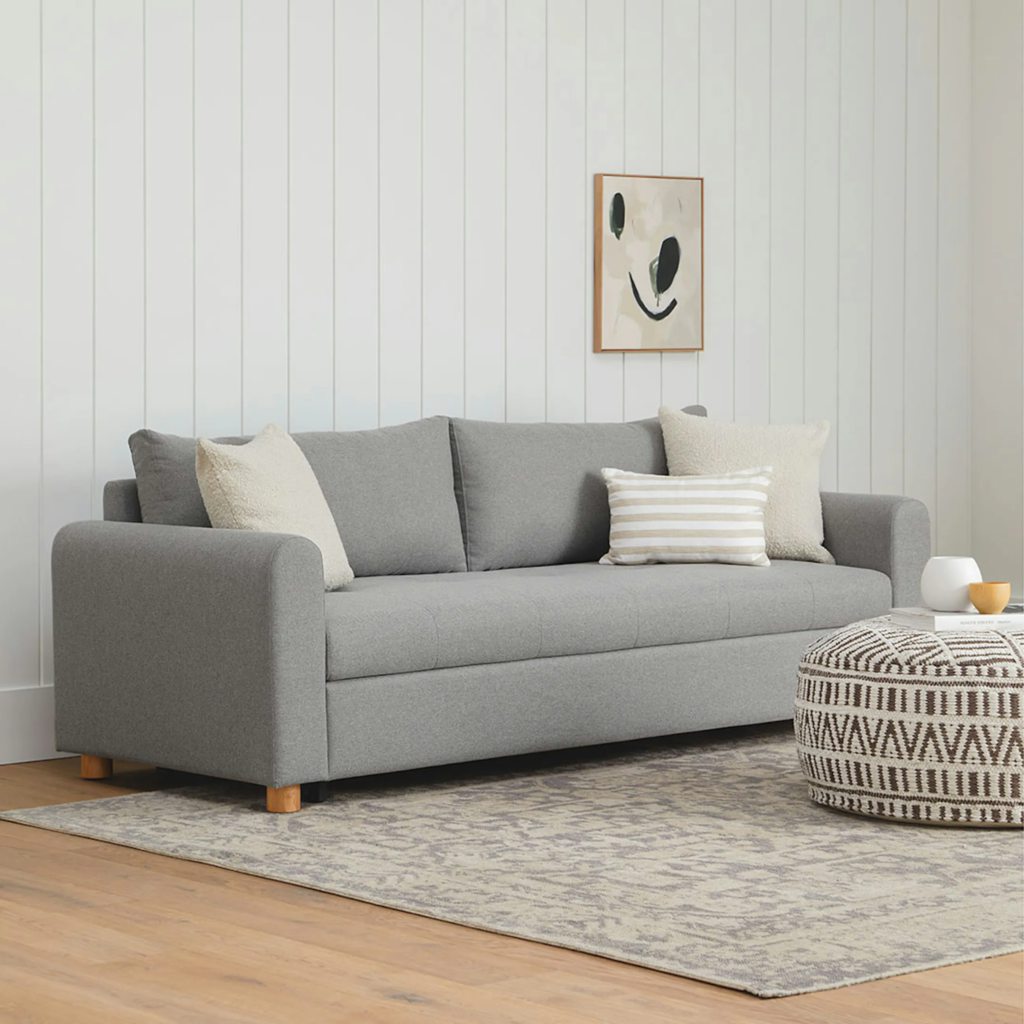 Gray upholstered sofa bed with throw pillows in a bright modern living room.