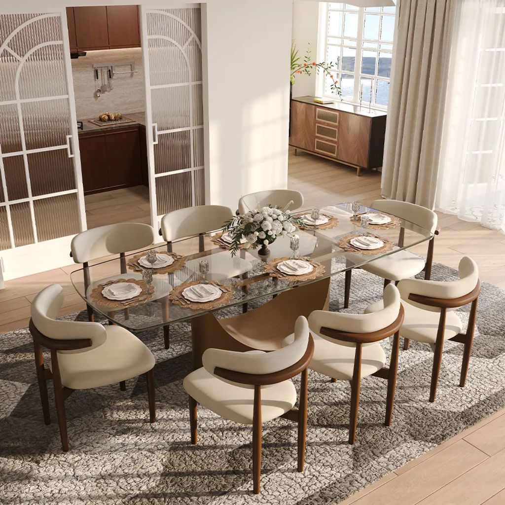 Rectangular glass designer dining table with a sculptural pedestal base and eight upholstered chairs in a bright modern dining room.
