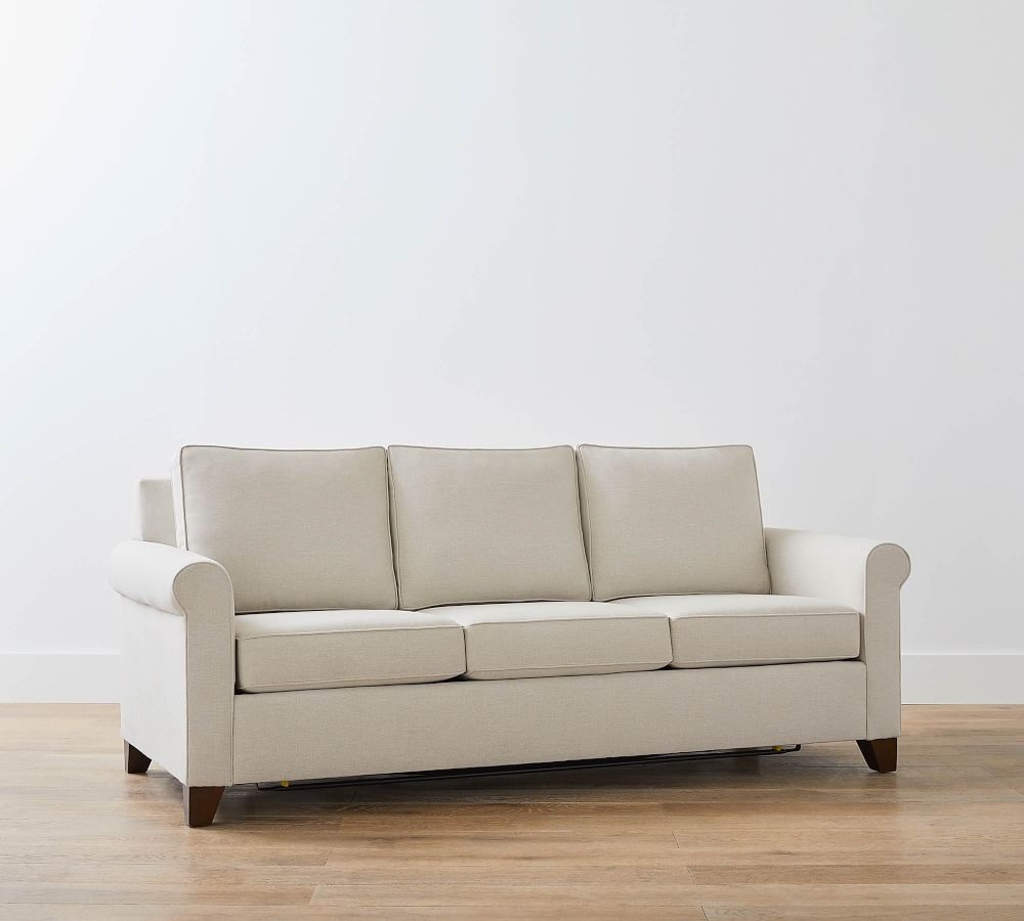 Beige roll-arm sleeper sofa with loose cushions on a light wood floor.