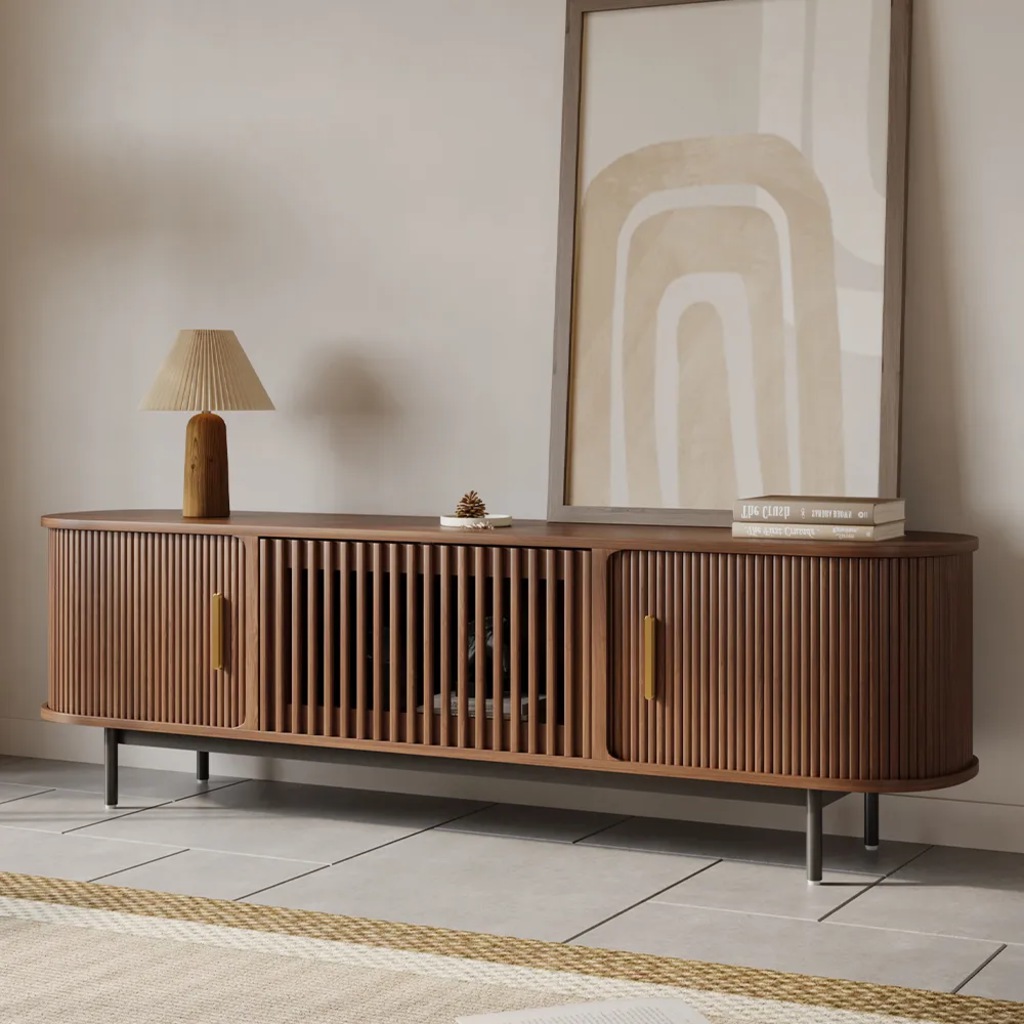 Walnut narrow TV stand with tambour doors, black legs, a table lamp, framed artwork, and stacked books.