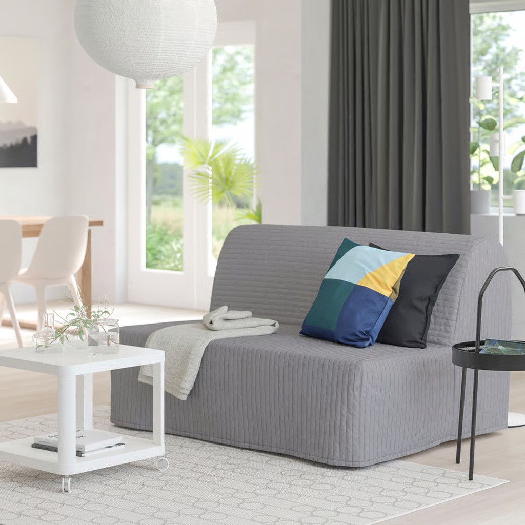 Gray fold-out sleeper sofa with a ribbed cover and throw pillows in a bright modern living room.