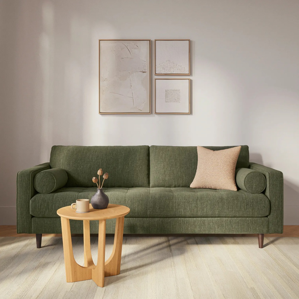 Green mid-century sofa with bolster pillows and a small wood table in a bright Airbnb living room