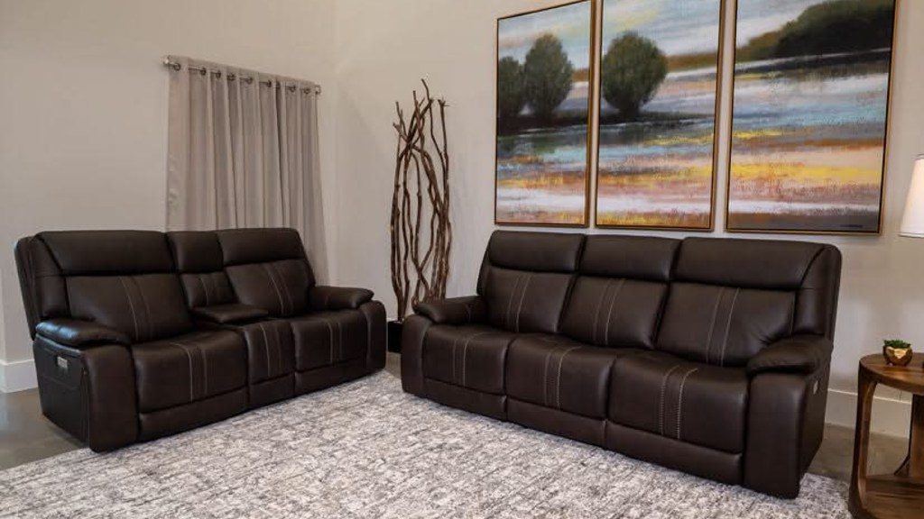 Dark brown leather reclining sofa and loveseat set arranged on a gray area rug in a traditional living room.