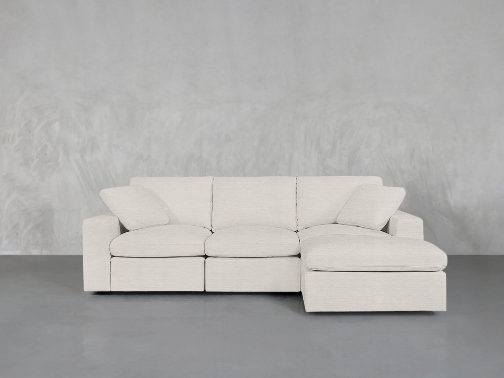 White L-shaped sectional sofa with a chaise and loose cushions against a gray wall.