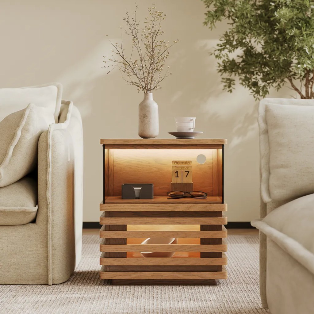 Tall dried branches in a textured vase on a wood side table with open storage between two cream upholstered chairs.