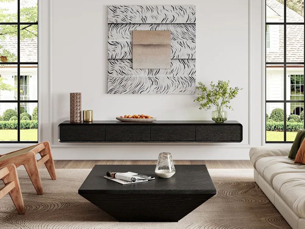 White living room with a black floating media console, black coffee table, cream sofa, wood accent chairs, and patterned neutral rug.