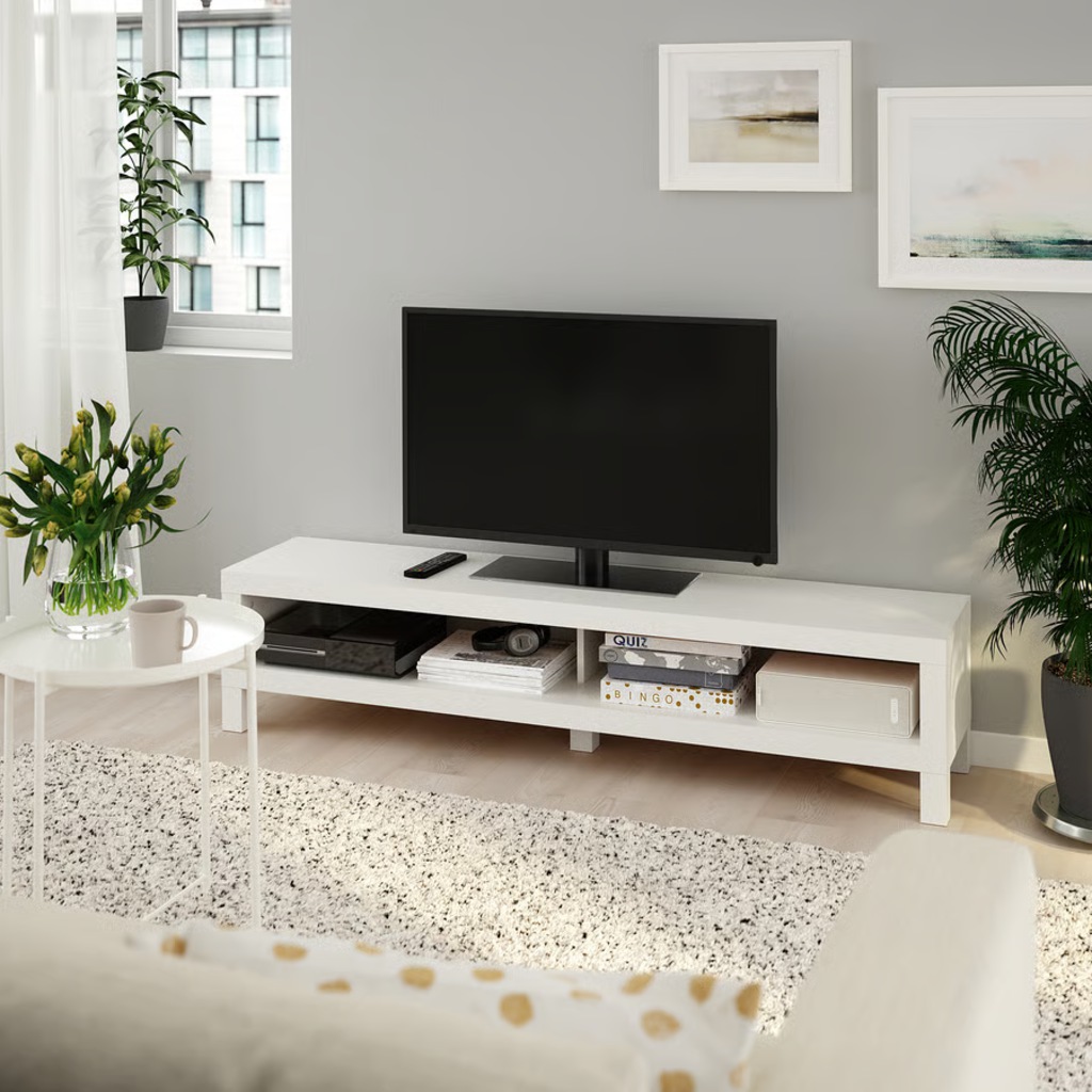 White low-profile narrow TV stand with open shelving and a flat-screen TV in a bright living room.