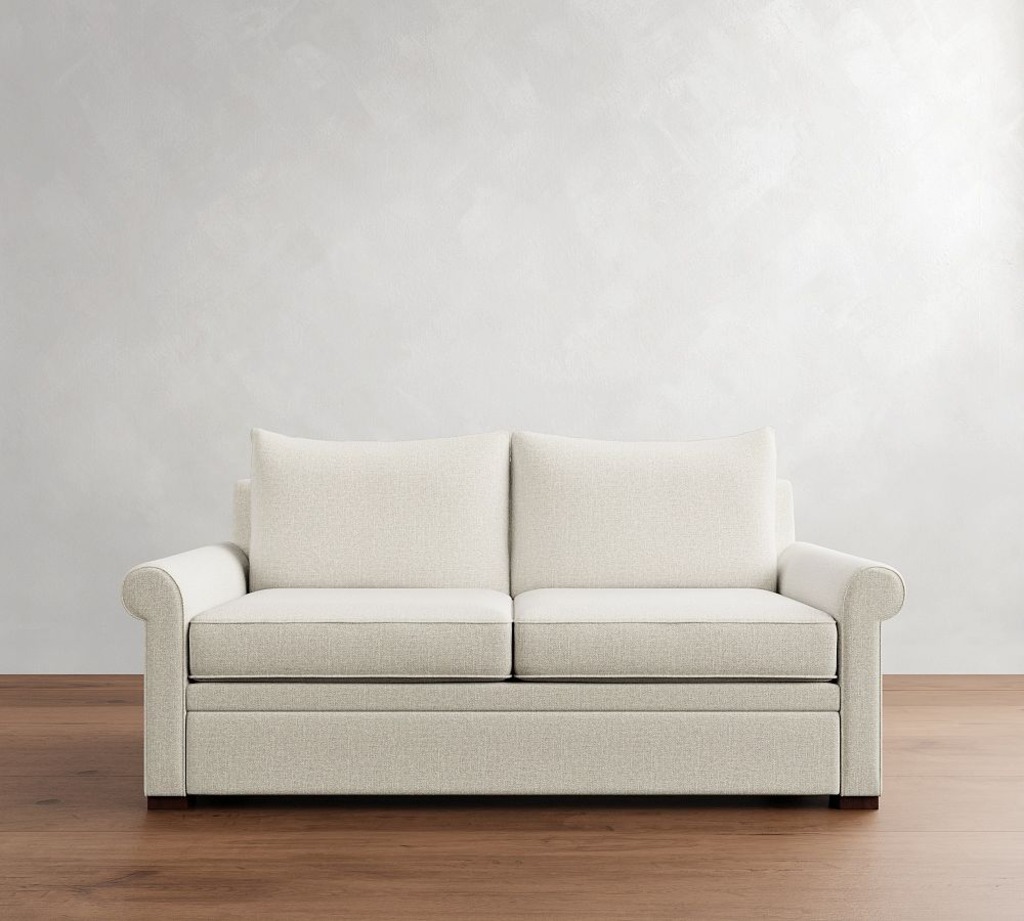 Cream two-seat sleeper sofa with rolled arms and loose back cushions against a white wall