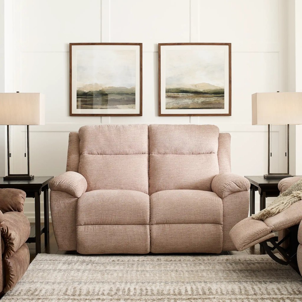 Plush blush two-seat reclining loveseat between matching lamps in a bright traditional living room.